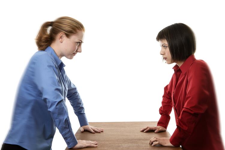 two woman stand over a table not looking very happy