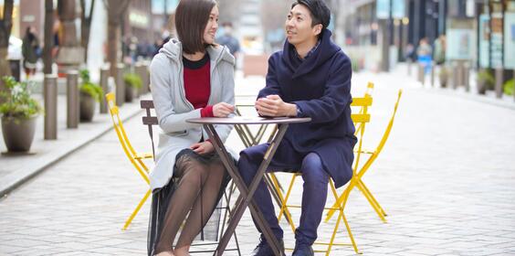 A young couple sitting at a table outside talking.