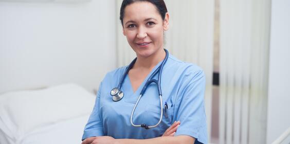 A nurse standing beside a bed smiling.