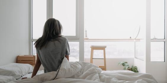 A woman sitting in bed looking out her apartment window.